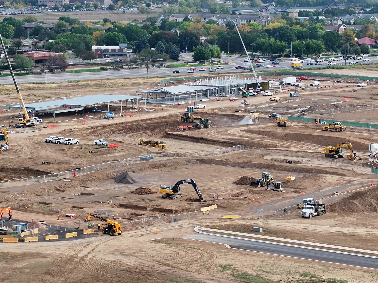 September 28 aerial view of excavation, grading equipment and a water truck spraying beside the commercial steel buildings